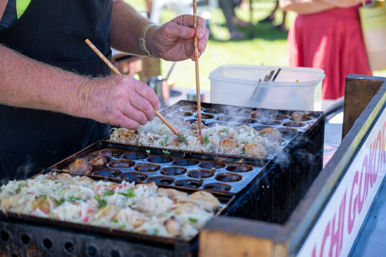 A vendor cooking fresh takoyaki on a hot plate at a festival food cart